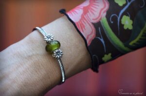 een dames armband met een crematie as verwerking in een olijfkleurige glasbedel en 2 zilveren bloem bedels